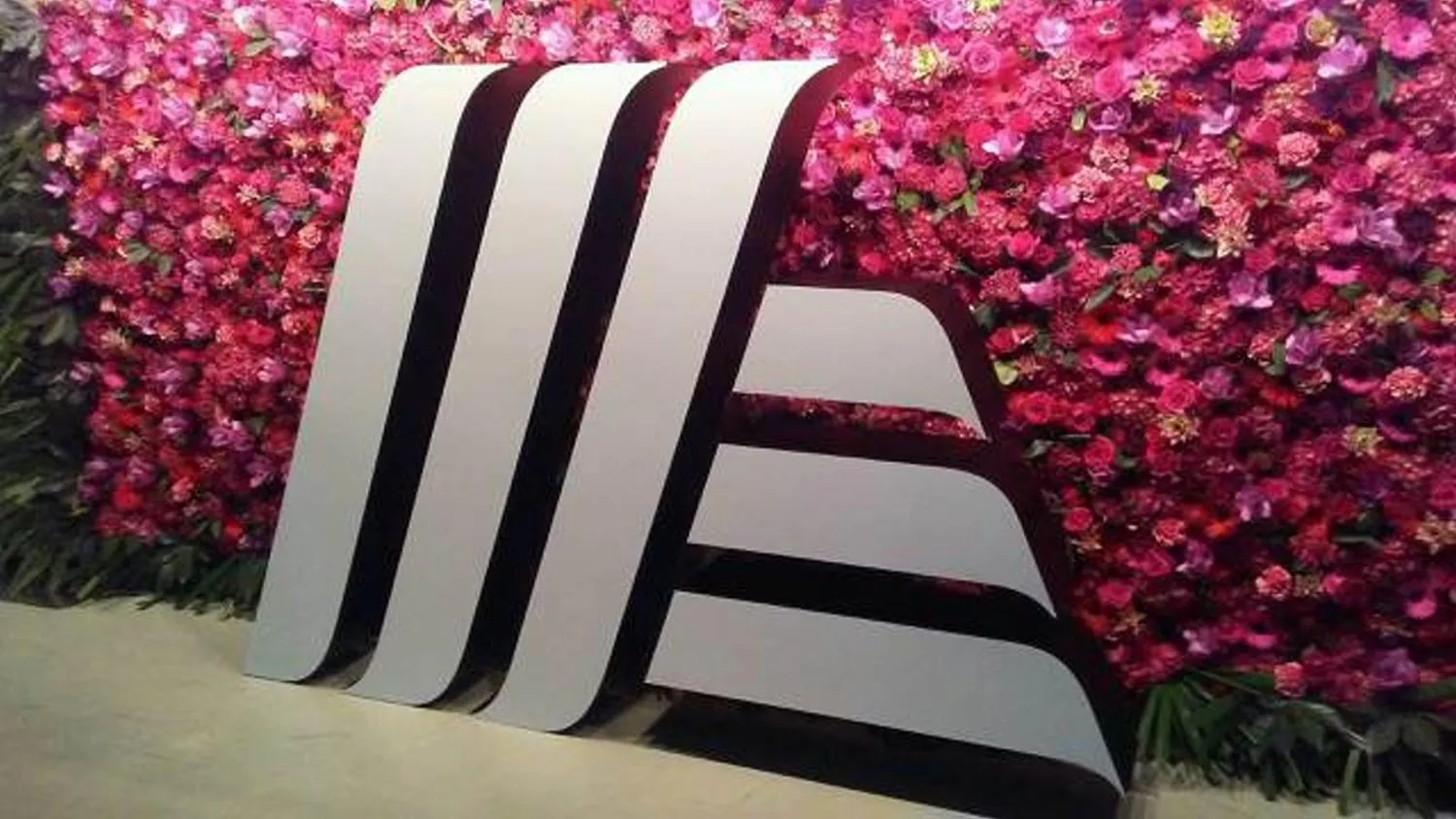 3D-Logo vor einer Blumenwand